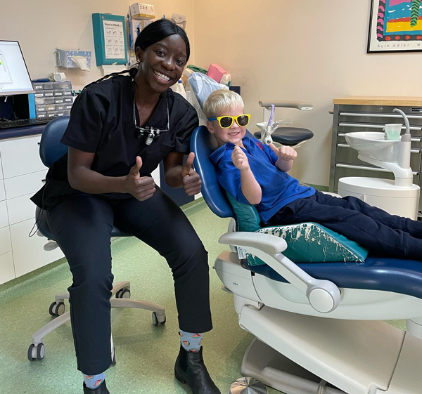 knightstreetdentists.com.au | Dental assistant giving a thumbs-up while a young child relaxes in the dental chair wearing sunglasses.