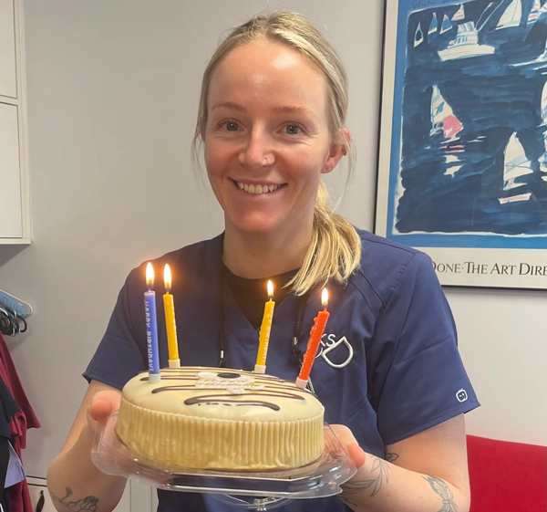 knightstreetdentists.com.au | Smiling dental staff member holding a small birthday cake with lit candles.
