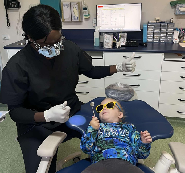 knightstreetdentists.com.au | Dental assistant interacting with a young child in the dental chair as the child wears sunglasses and looks up.